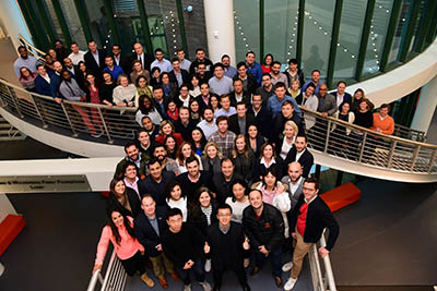 A large group of EMBA students gather on a stair case for a group image