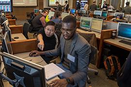 Students gather around a computer in the mock trading room