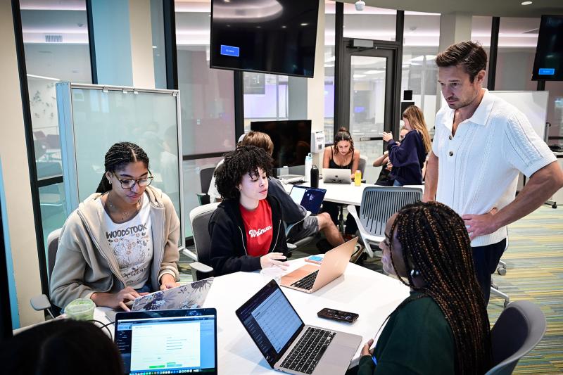 A teacher supervises students working on laptops in a GWBC classroom.