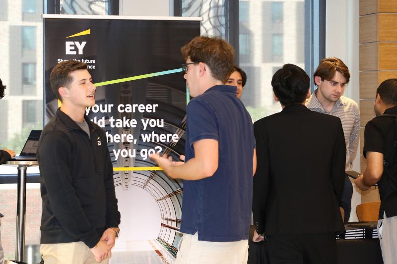 Career fair with students talking near an EY banner.