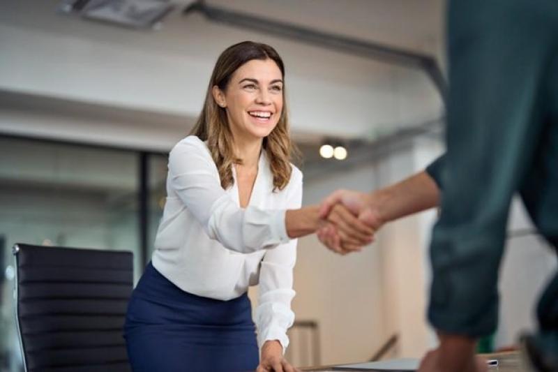 Smiling woman in white shirt and blue skirt shaking hands in an office.