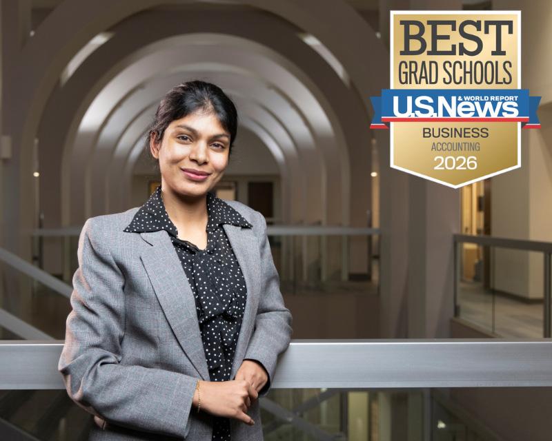Woman in a grey suit and polka dot shirt smiles in a hallway with a U.S. News & World Reports Best Accounting program 2026 badge.